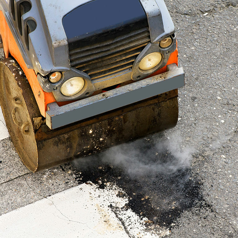Ace Paving steamroller compacting fresh asphalt for pothole repair in Atlanta, with visible steam rising from the hot surface.